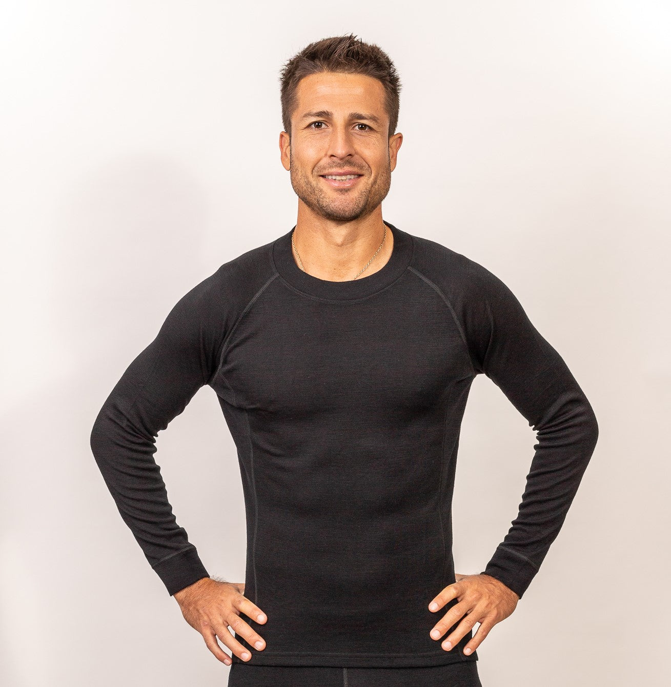 Hombre sonriente con camiseta negra de manga larga, posando con confianza sobre fondo claro y espacio neutral.