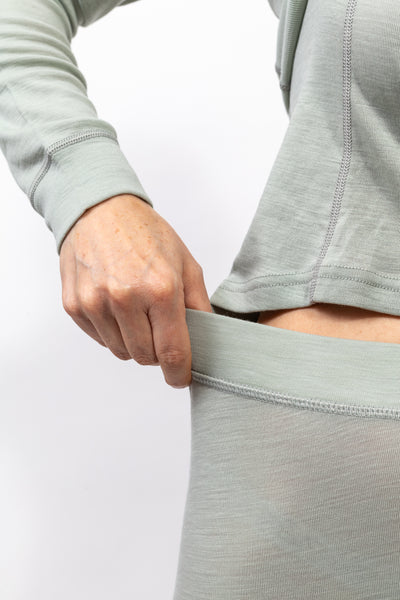 Mano ajustando la cintura de pantalón de tela suave color verde claro con camiseta a juego.